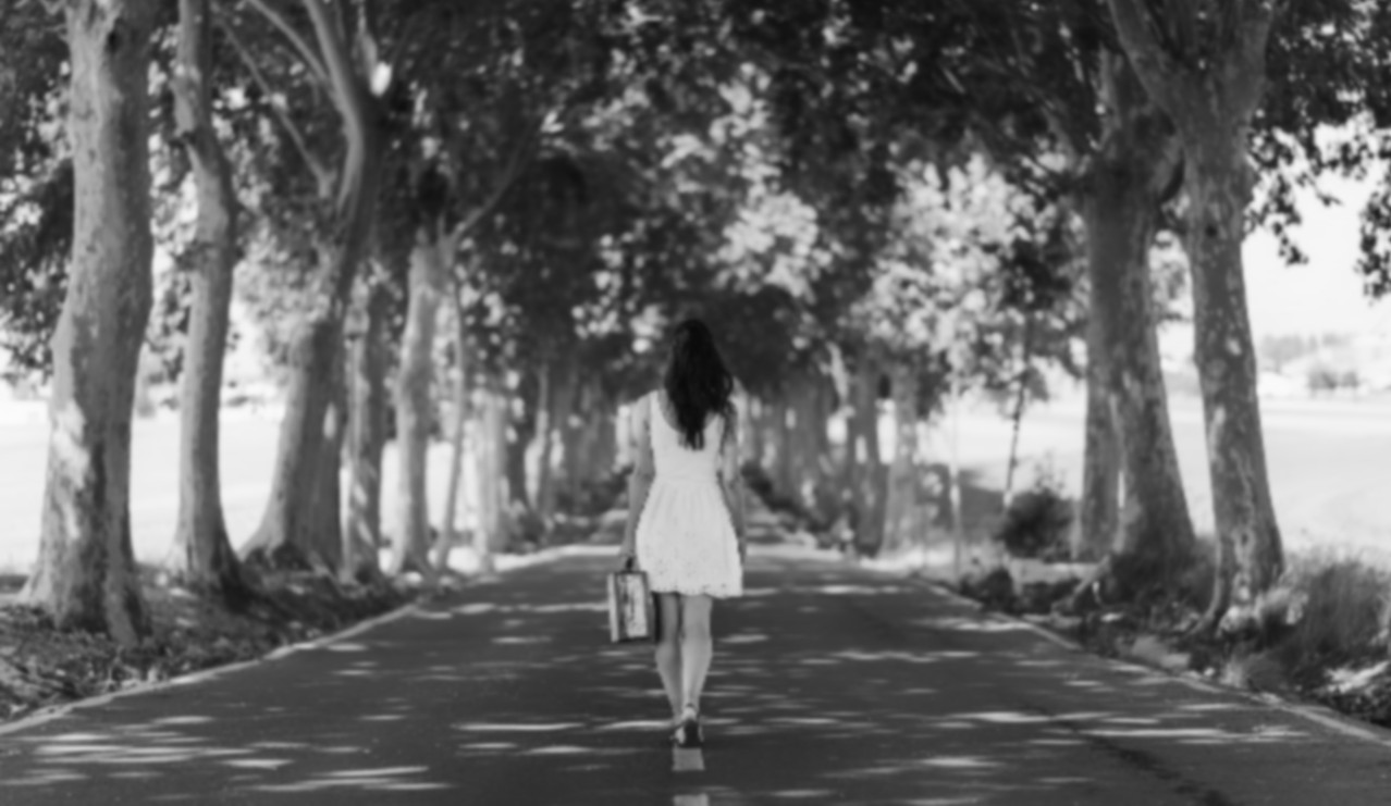 woman walking down tree lined path with suitcase